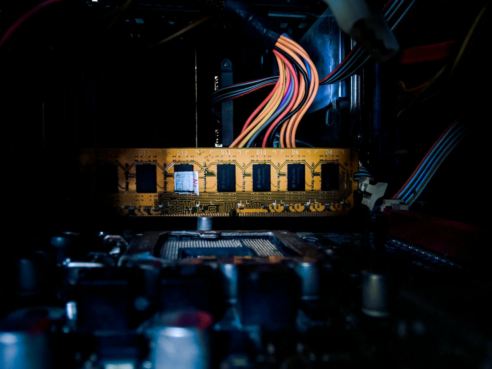 Detailed image of a computer circuit board with colorful cables and electronic components in low light.